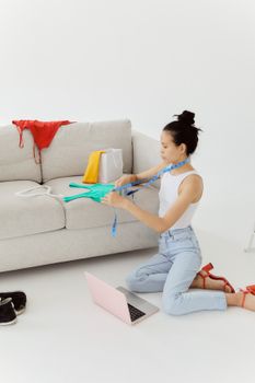 Young woman measuring clothes for online shopping with laptop on floor.