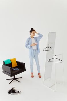 Woman in light blue attire fixing her hair in front of a tall mirror indoors.