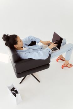 Woman lounging in a chair working on a laptop at home, captured at a creative angle.