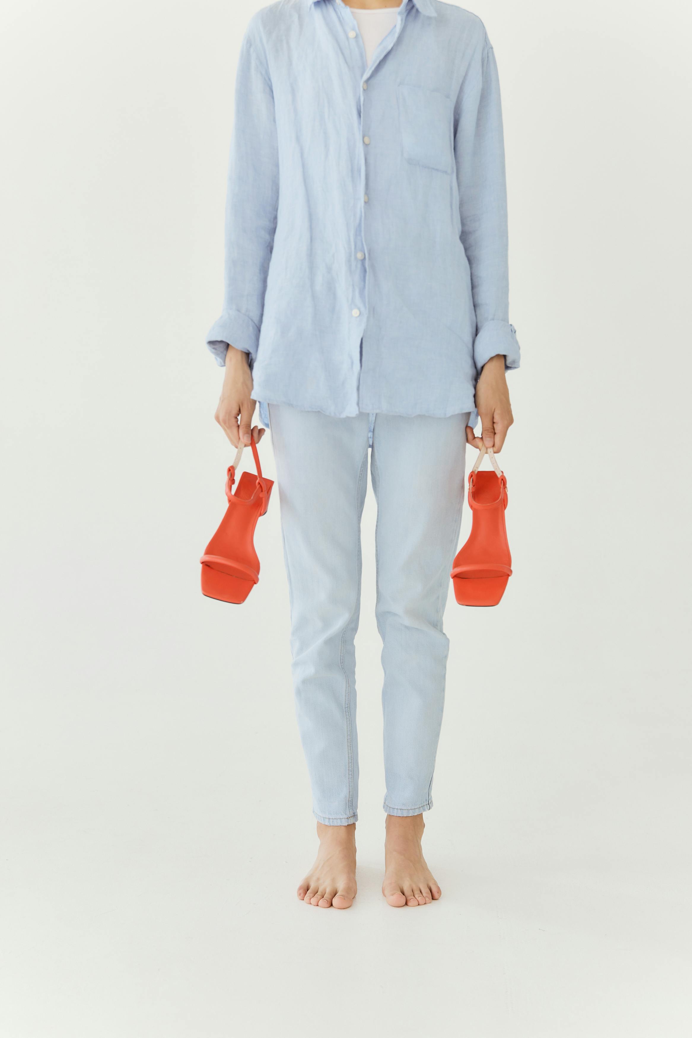 Person in light blue outfit holding red sandals. Minimalist and stylish.