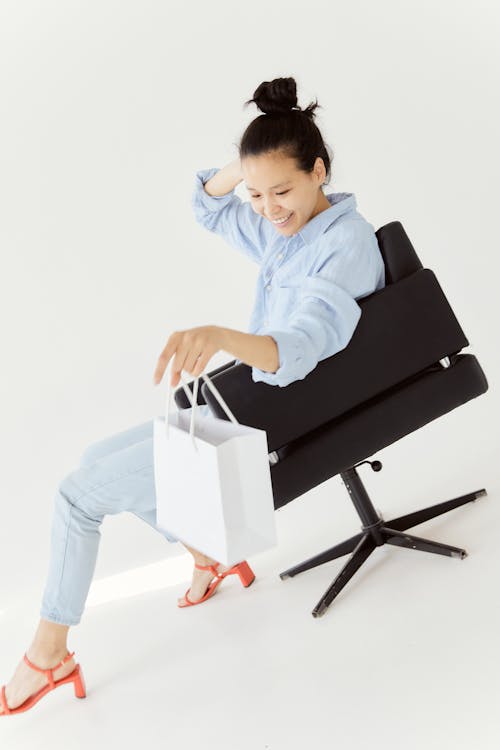 Woman Holding White Paper Bag While Sitting on Black Chair 