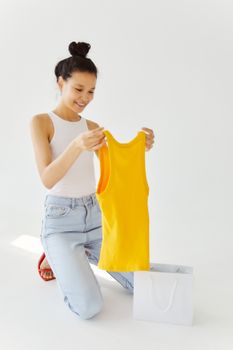 A young woman joyfully unpacks a yellow top from a shopping bag indoors.