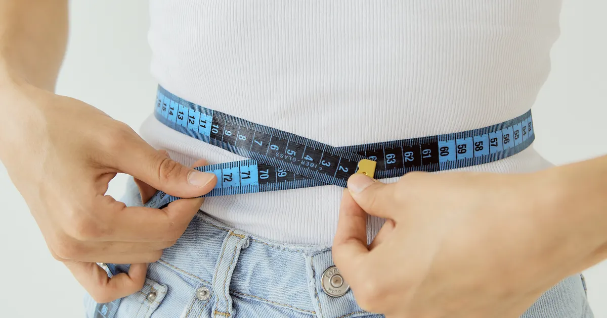 Person in a white T-shirt measuring their waist with a tape measure