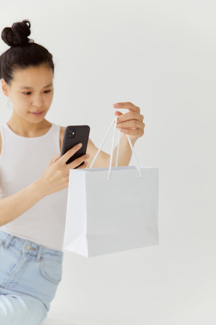 Woman In White Tank Top Taking Photo Of A White Shopping Bag