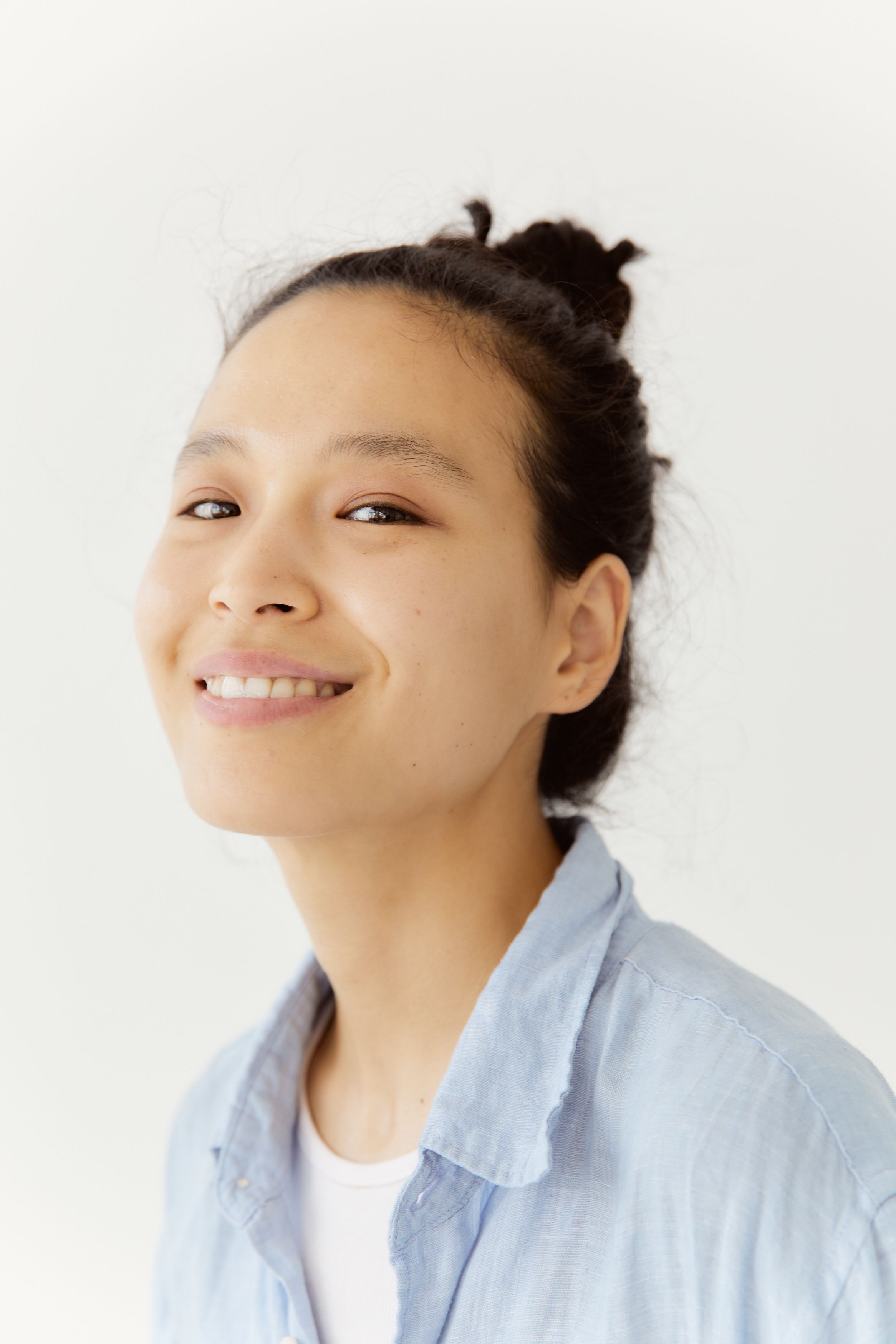Close-up portrait of a smiling woman with hair tied back, wearing a light blue shirt.