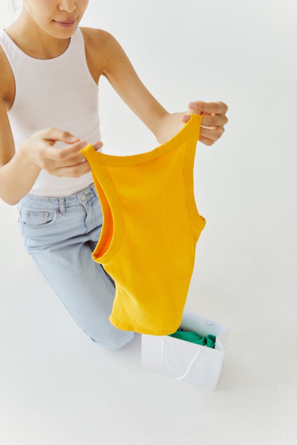 Woman in Yellow Tank Top and Blue Denim Jeans Holding Yellow Tank Top
