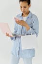 Woman Using her Smartphone While Holding a Shopping Bag and a Laptop