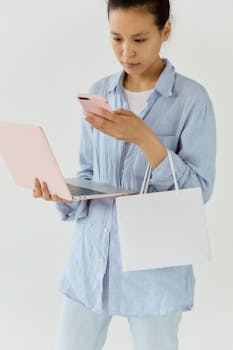 Woman in casual attire shopping online using a laptop and phone indoors.