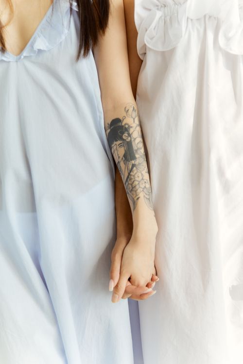 Free A close-up photo of two women holding hands, showing a tattoo design on one arm. Stock Photo