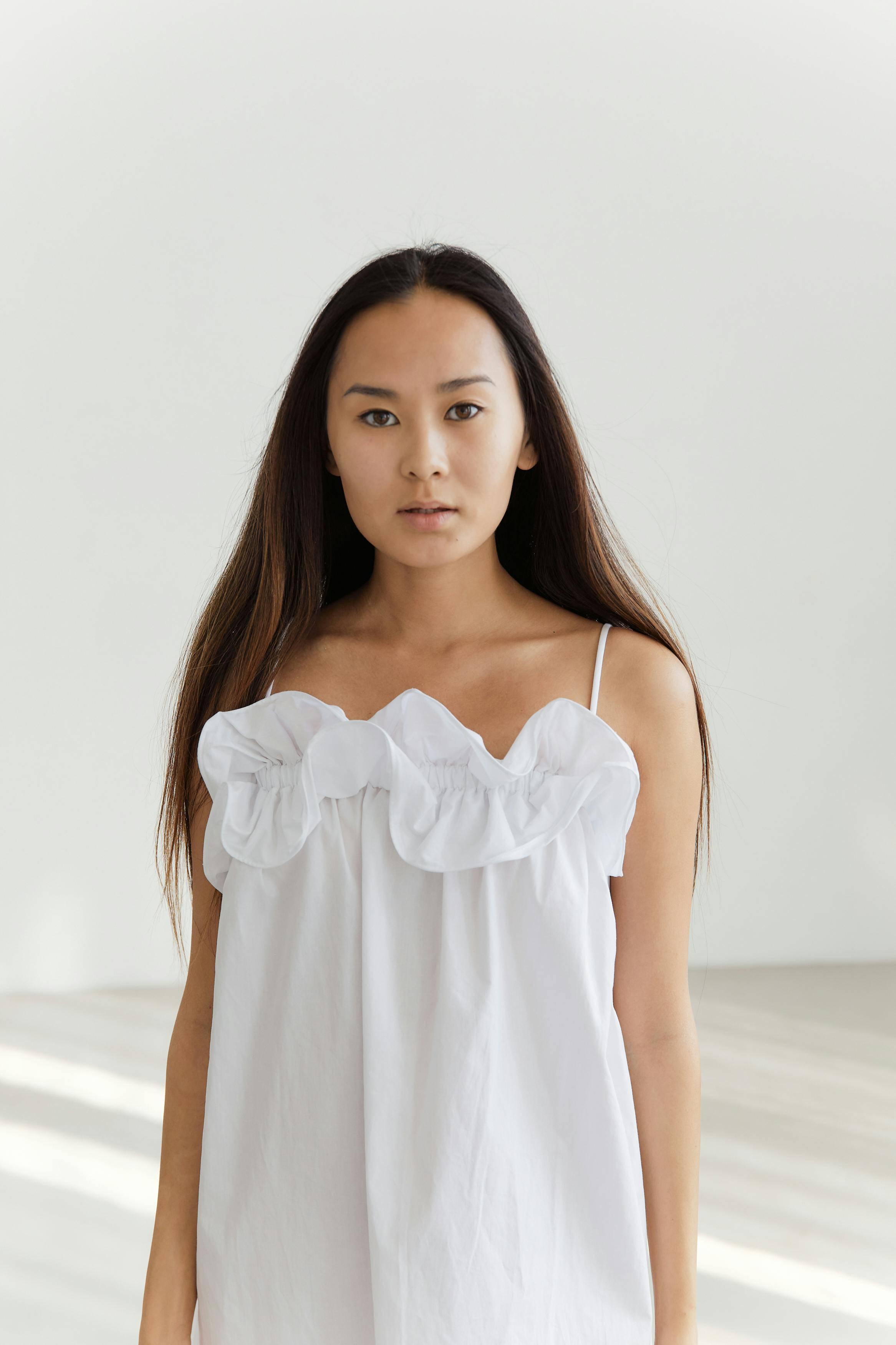 Portrait of an Asian woman wearing a white dress in a minimalist indoor setting.