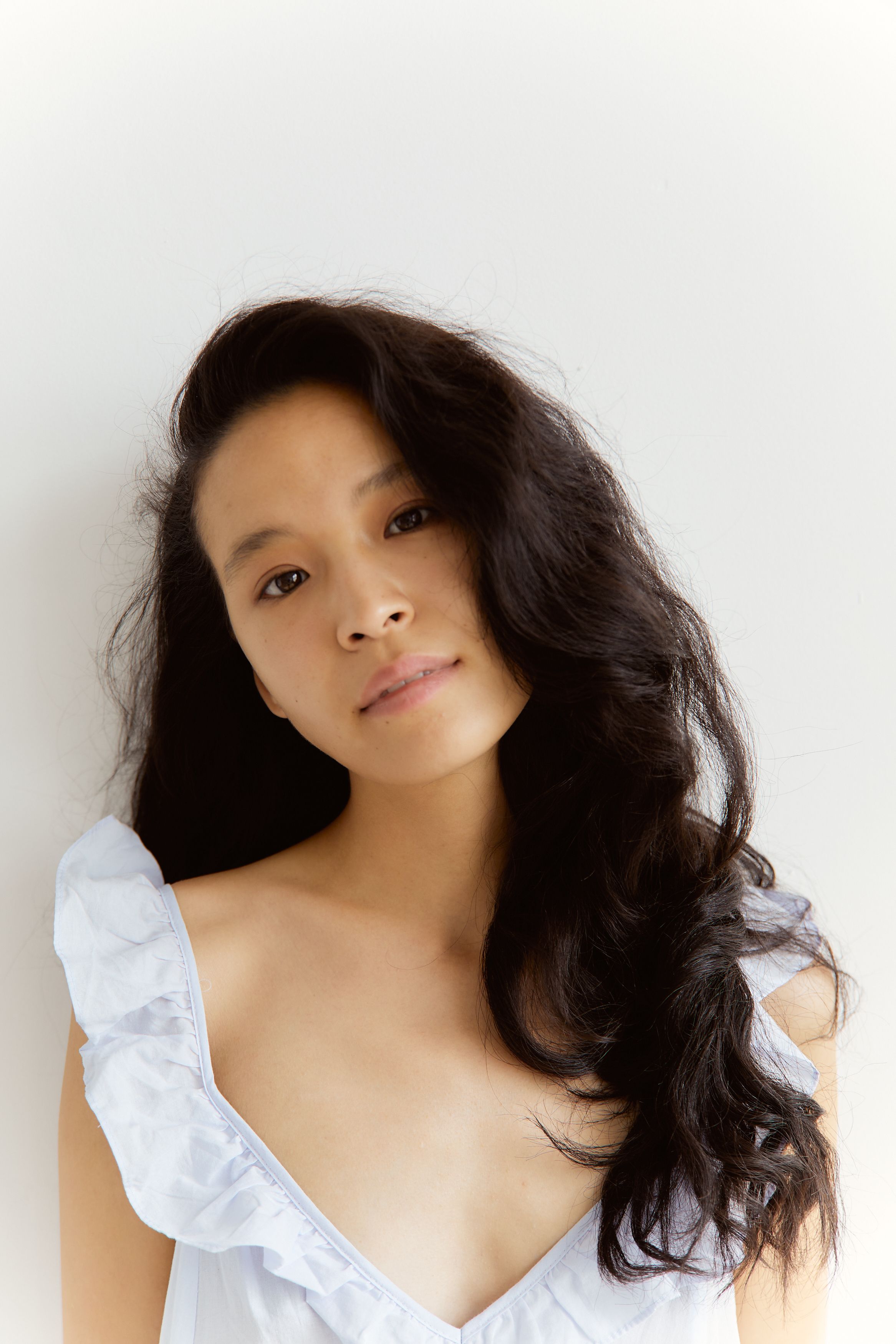 Serene portrait of an Asian woman with natural hair and no makeup against a white background.