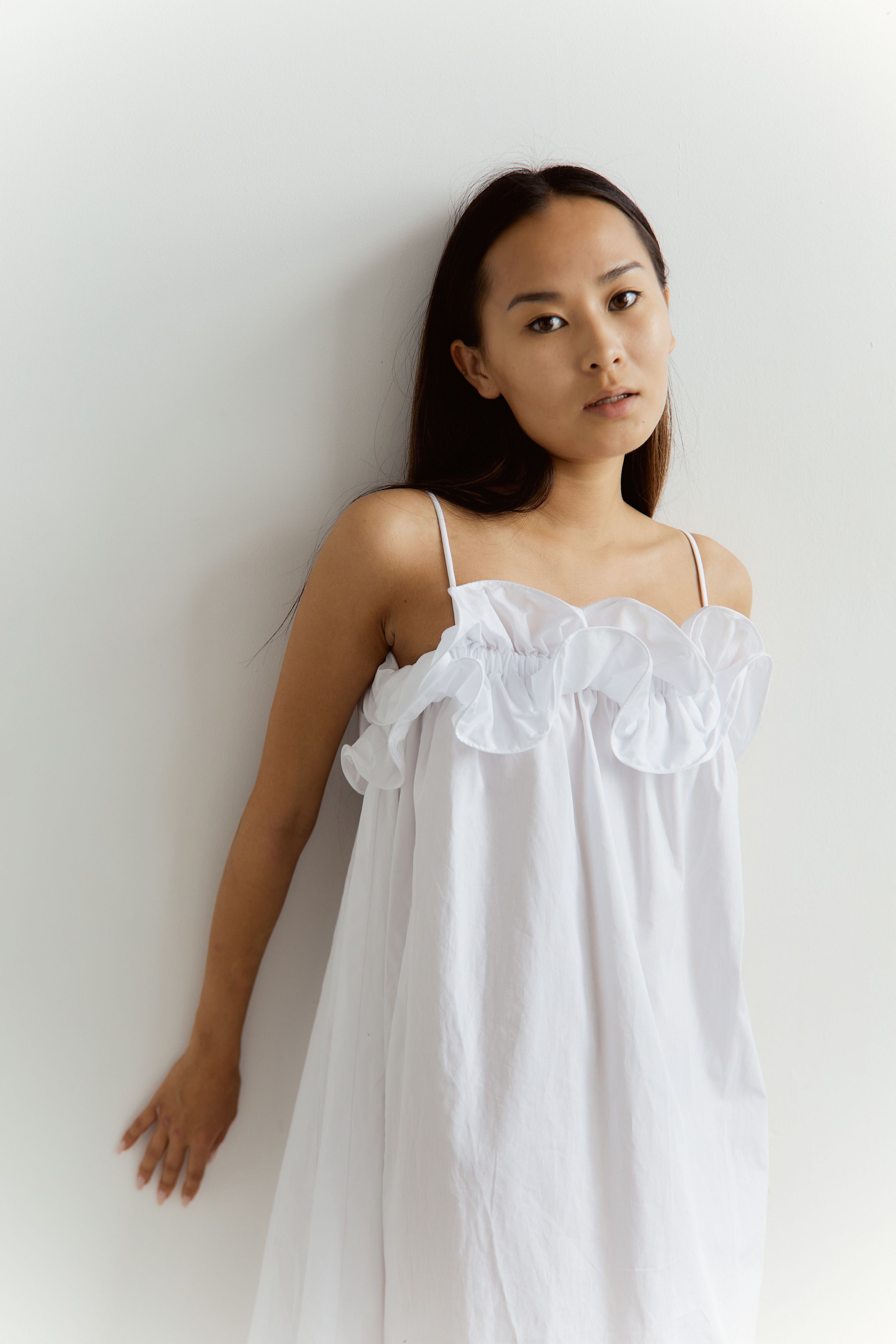 Beautiful portrait of a young woman in a white dress against a plain background.
