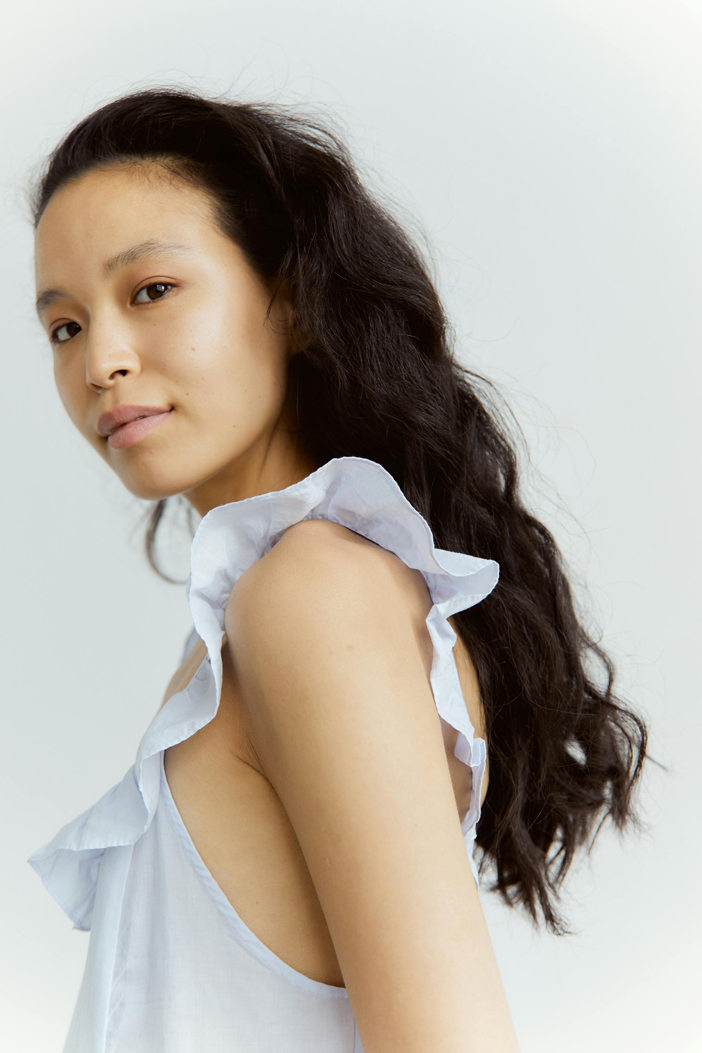 Elegant portrait of a young Asian woman posing in a studio with soft lighting and fashionable attire.