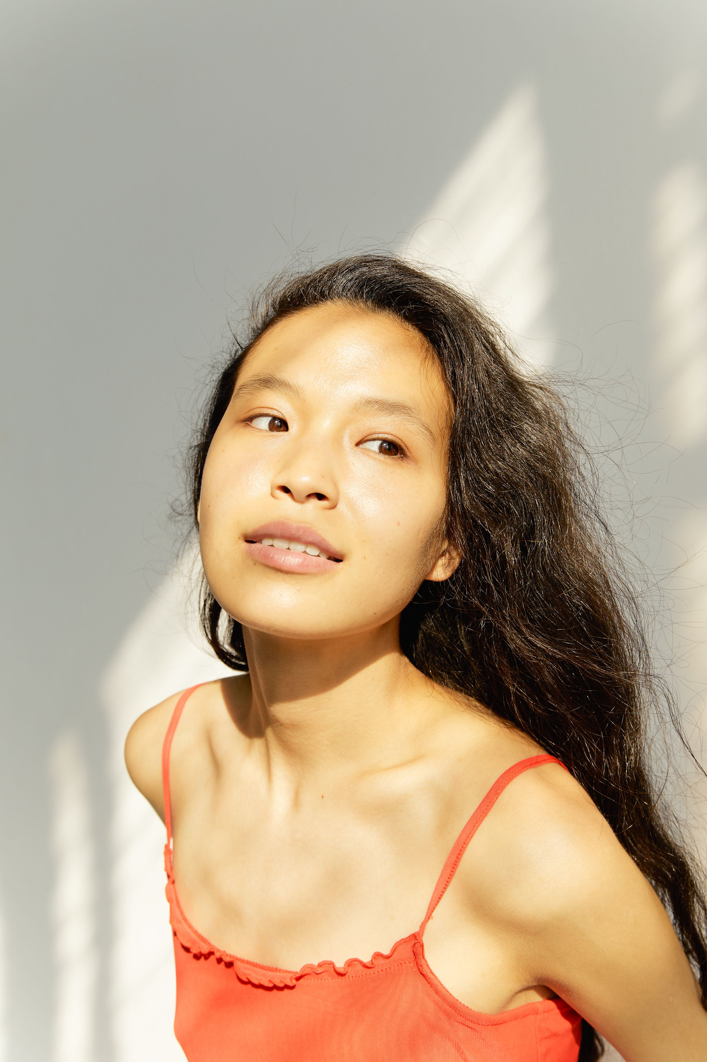 Portrait of a young woman in a red top, illuminated by natural lighting, looking upwards.