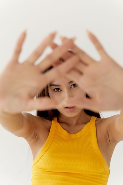 Artistic portrait of a woman in a yellow top posing with hands in focus.