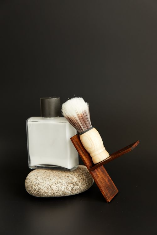 Free Close-up of a minimalist grooming kit featuring a shaving brush and perfume bottle on a stone. Stock Photo