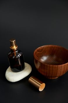 A minimalist setup featuring a glass spray bottle, wooden bowl, and pebble against a dark background.