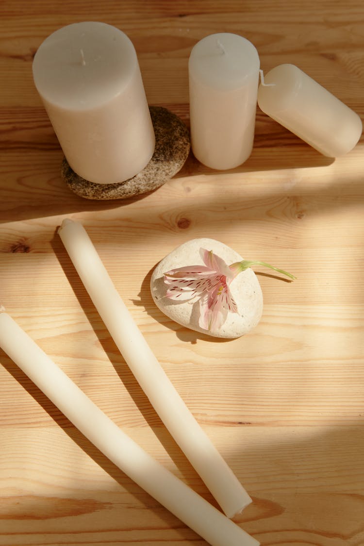 White Candles Beside Rock With Flower On Brown Wooden Table