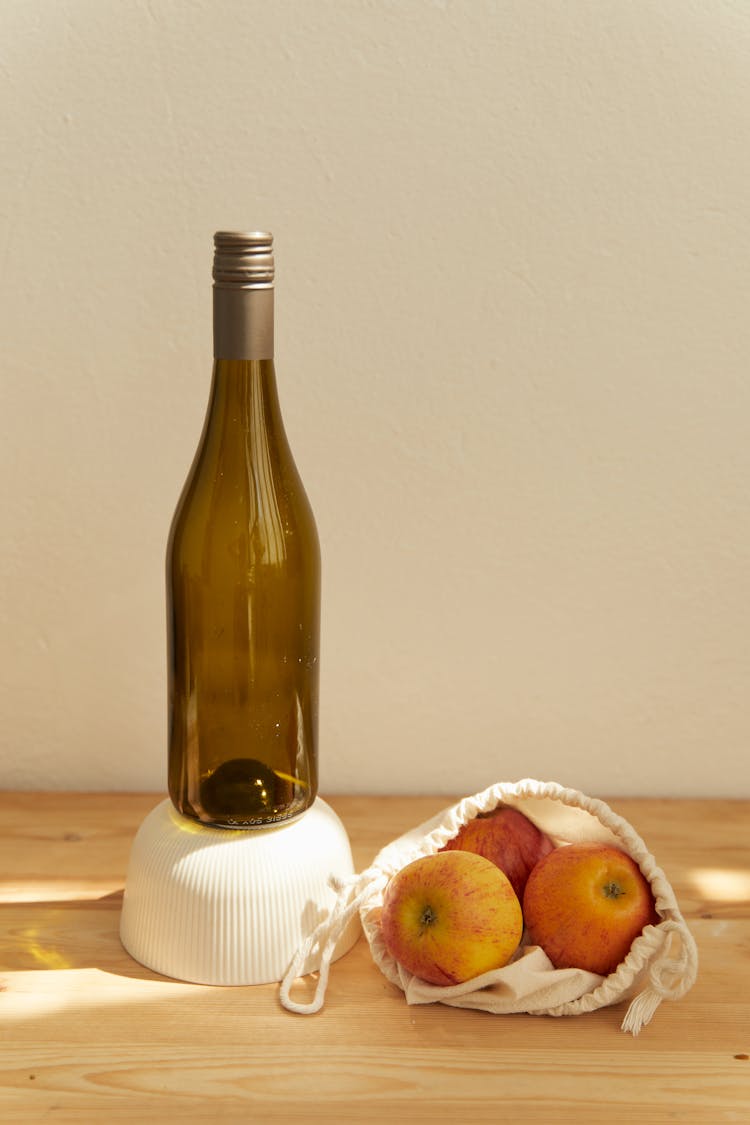 A Wine Bottle Besides A Bag Of Apples