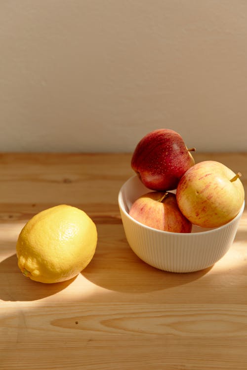 Red Apple Beside Yellow Lemon Fruit on White Ceramic Bowl