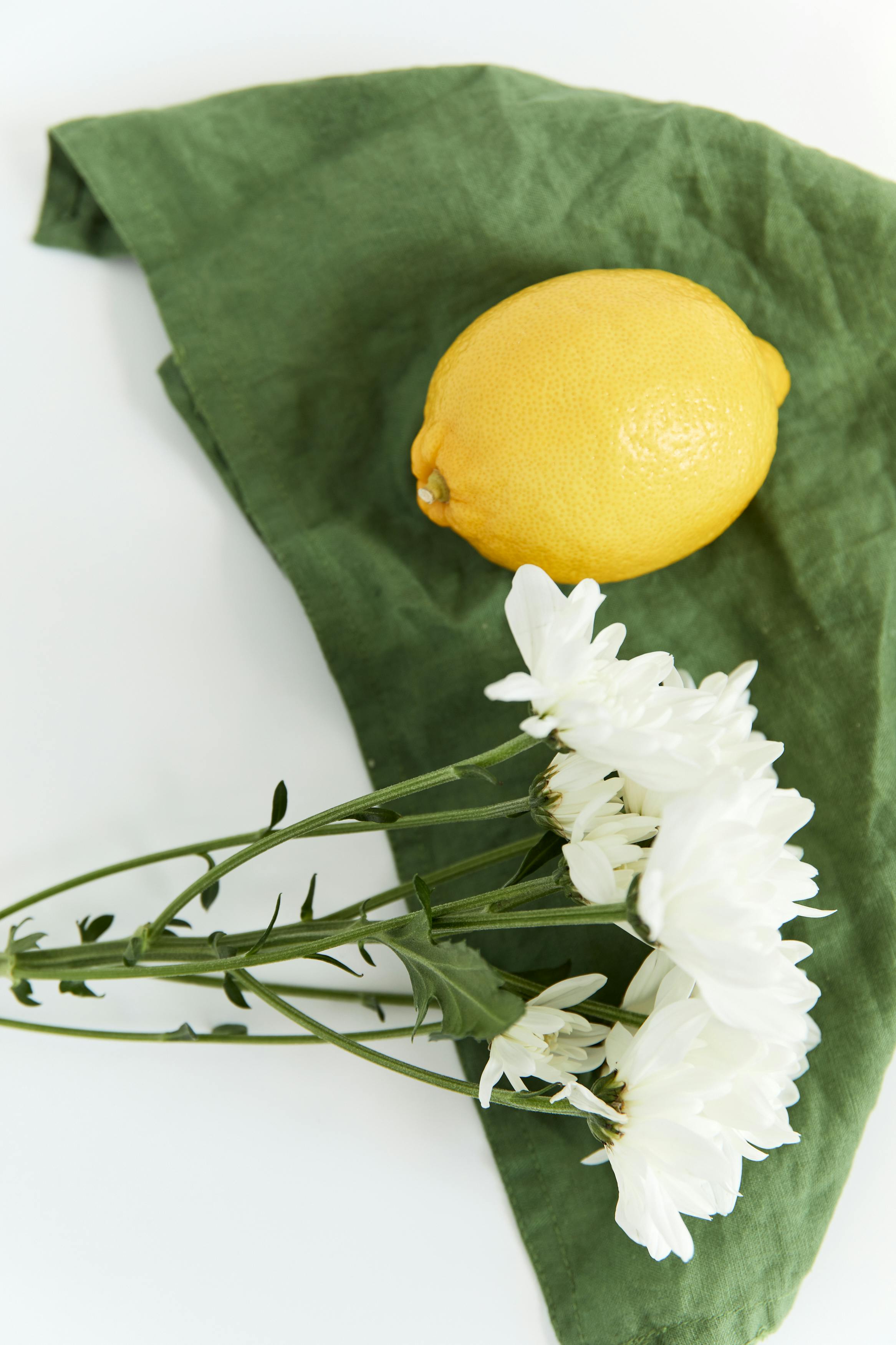 A bright yellow lemon and white flowers on green fabric, creating a vibrant still life.