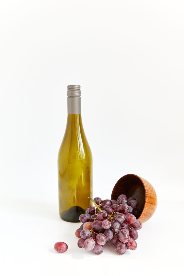 Unlabelled green wine bottle beside a bowl of red grapes on white, photo by Darina Belonogova on Pexels