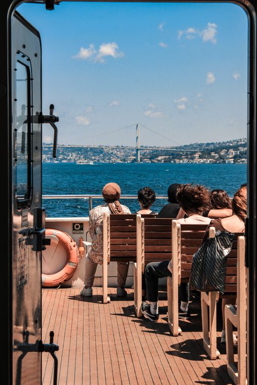 Free People seated on a cruise enjoying the scenic view of the Bosphorus Bridge in Istanbul under a clear blue sky. Stock Photo