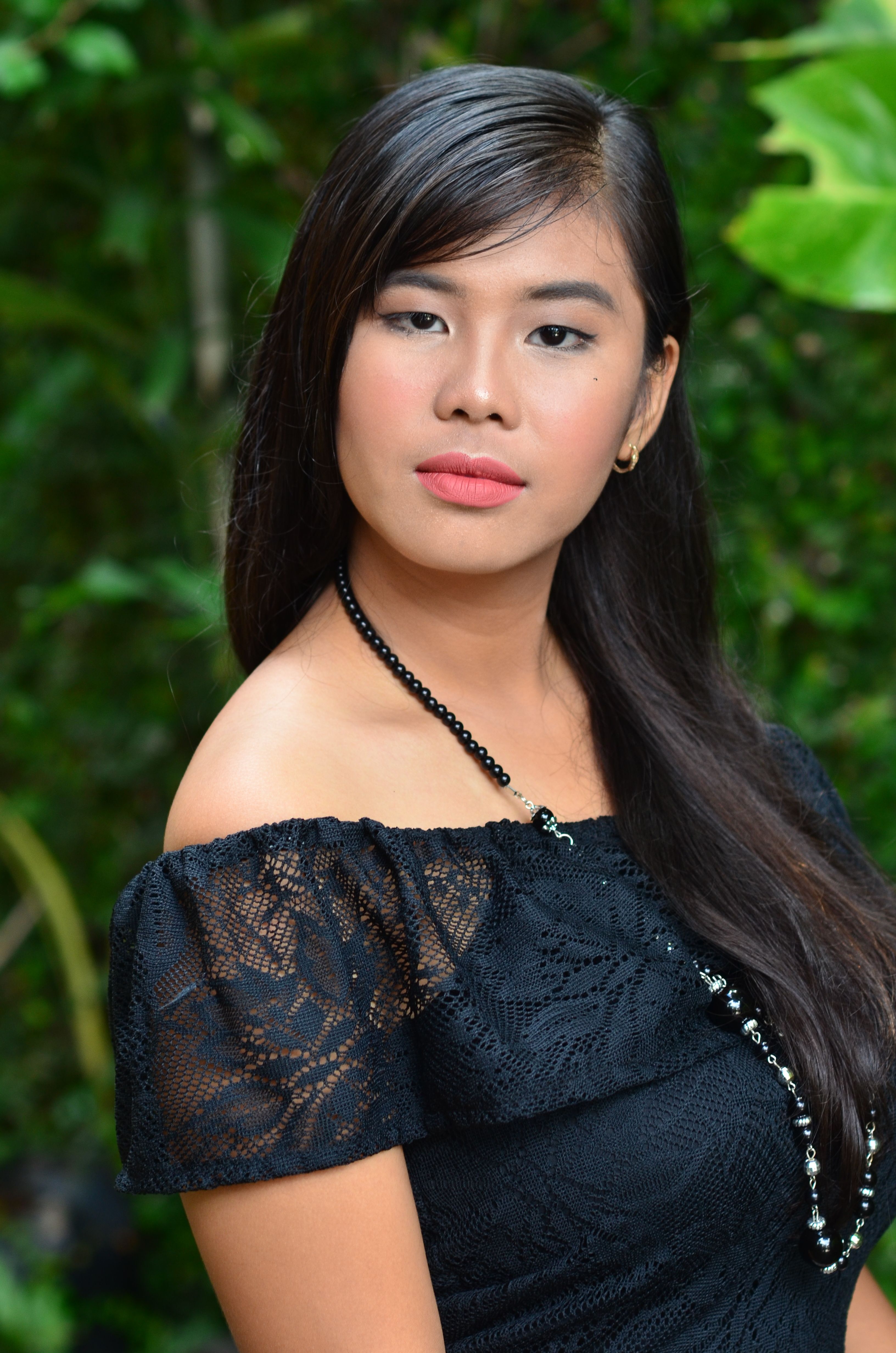 Stunning portrait of a woman in a black lace dress set outdoors in lush greenery.