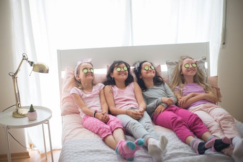 Free Girls in Pajamas with Cucumbers on Eyes Sitting on Bed Stock Photo