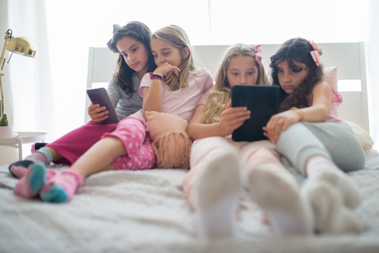 Children Sitting On Bed While Using Gadgets