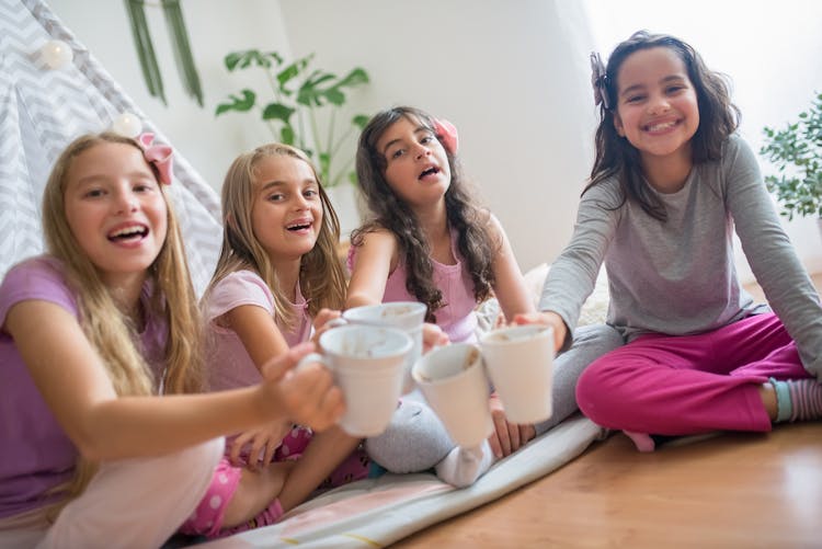 Girls In Pajamas Sitting On Wooden Floor Holding White Ceramic Cup