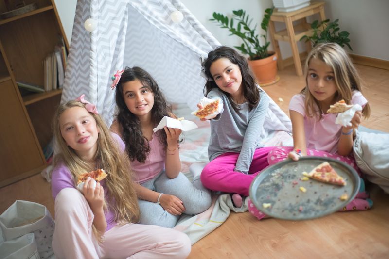 Young girls sitting on the floor enjoying pizza together at a party