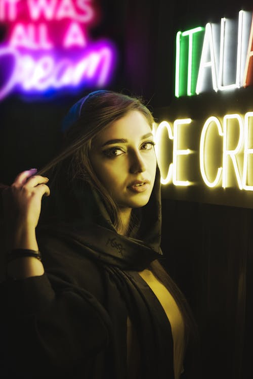 Woman Touching Her Hair Near a Neon Sign