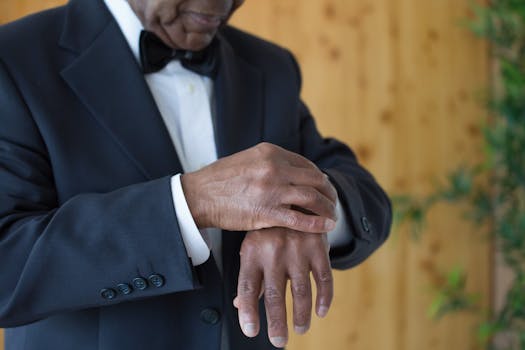 Close-up of a black man in a formal suit adjusting his sleeve indoors, conveying elegance and preparation.
