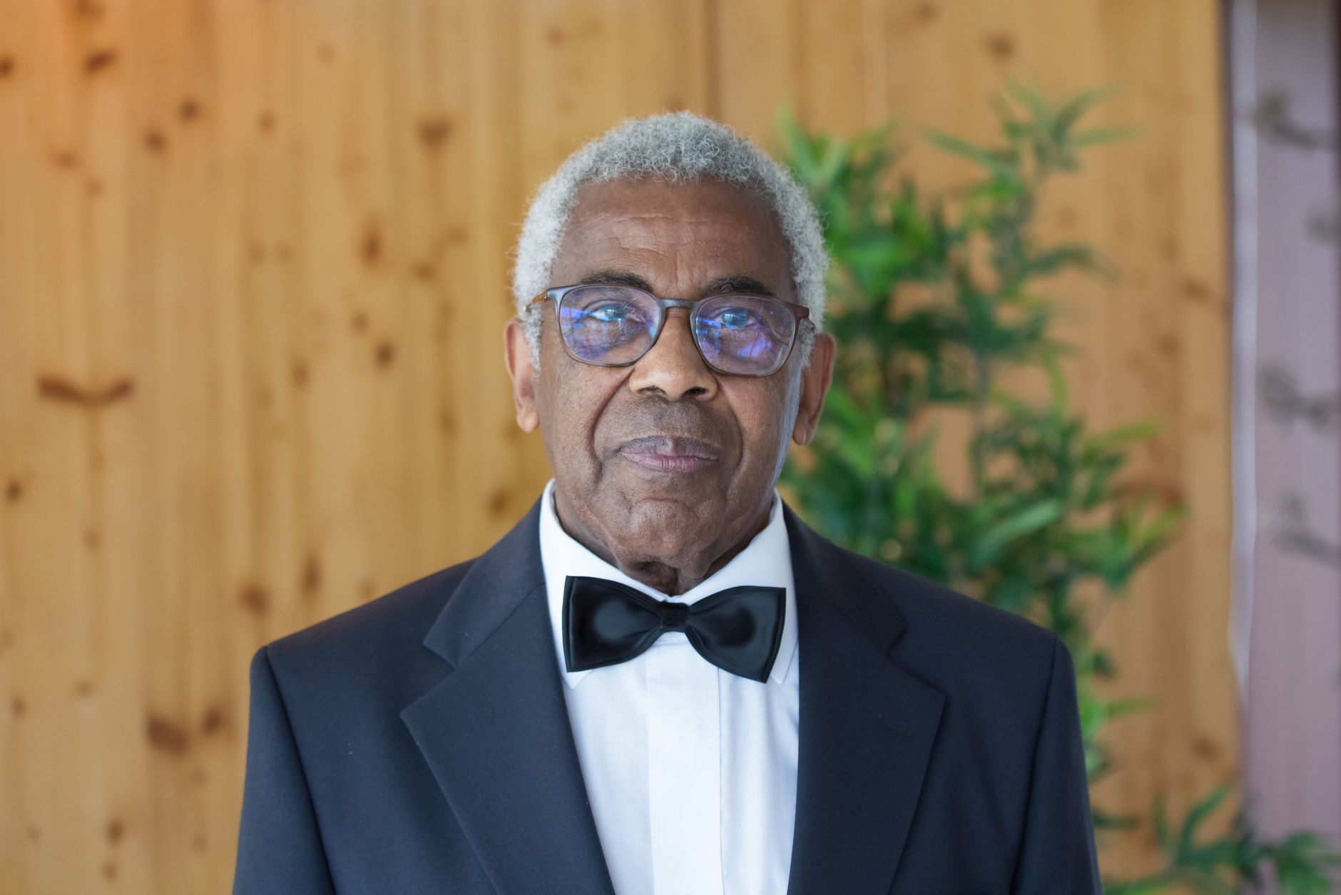 Distinguished elderly man in a black suit and bowtie indoors, exuding elegance.
