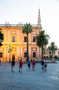 A group of people walking near a historic building with palm trees in Seville, Spain, during daylight.