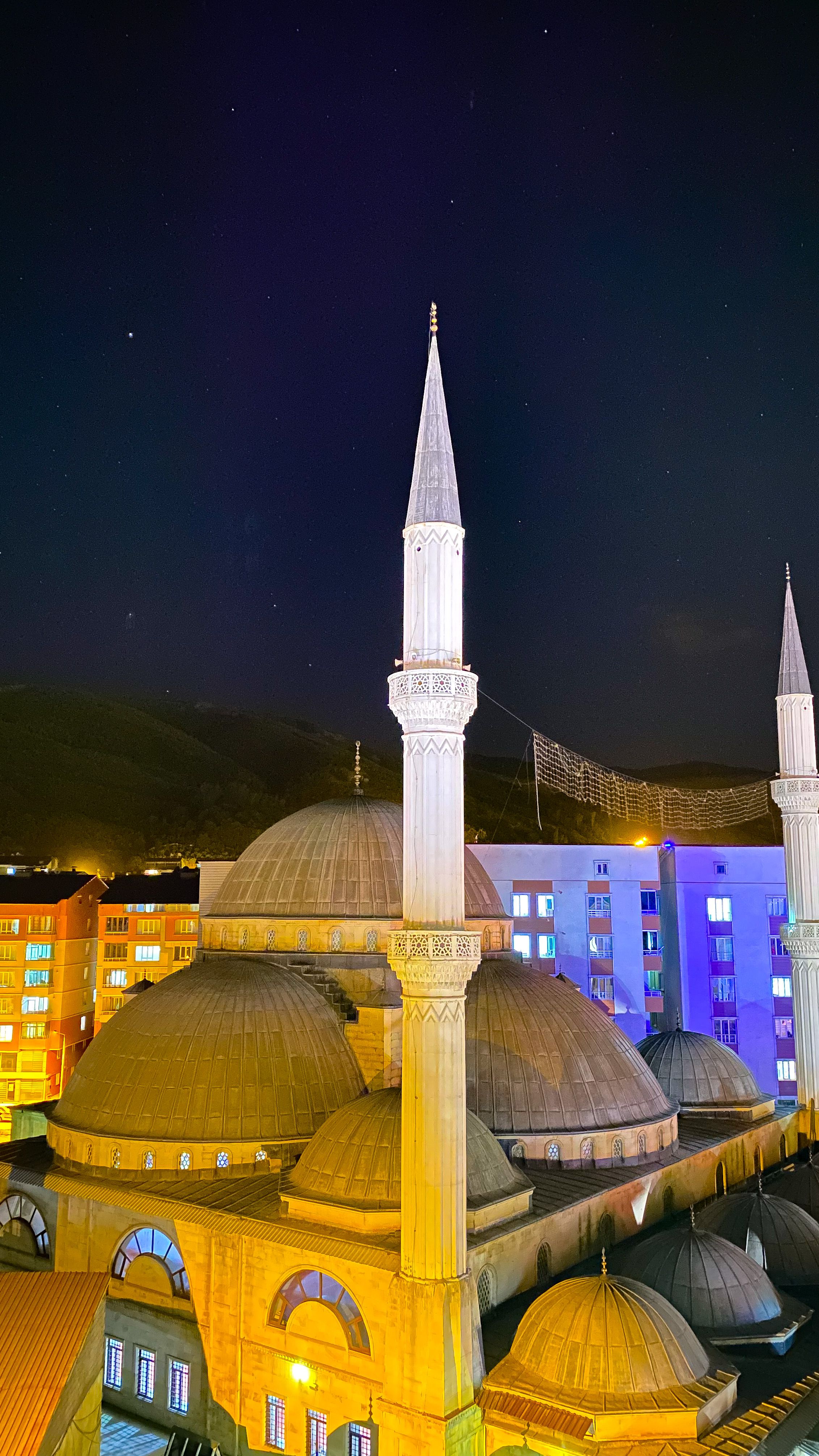Brightly lit mosque with domes and minarets against a starry night sky.