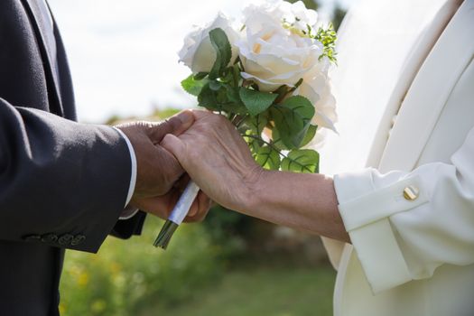 A romantic moment with an elderly couple holding hands during their outdoor wedding ceremony, showcasing love and togetherness.