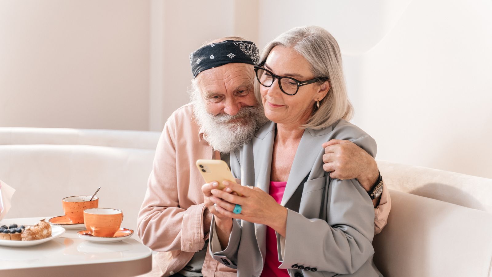 Two people looking at a smartphone together beside cups in a café