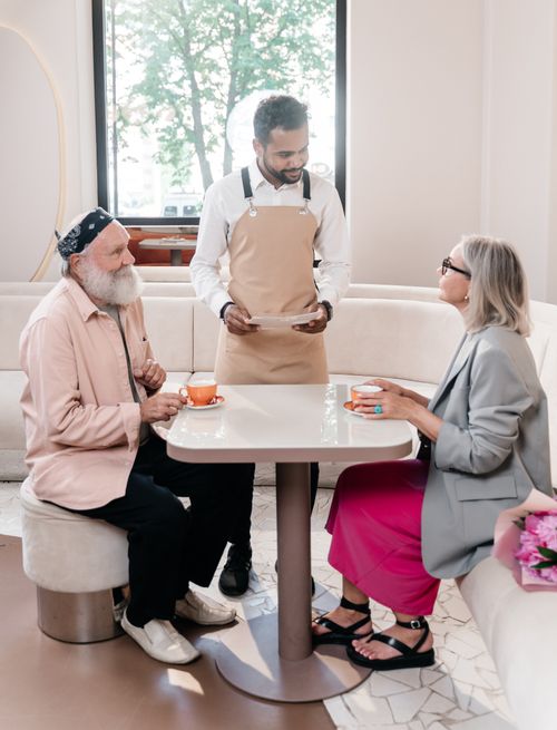 Free Senior couple enjoys coffee served by waiter in a cozy restaurant setting. Stock Photo