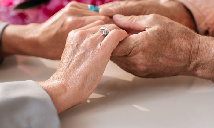 Mãos de familiar e idoso entrelaçadas com flores, presença e afeto no cuidado paliativo
