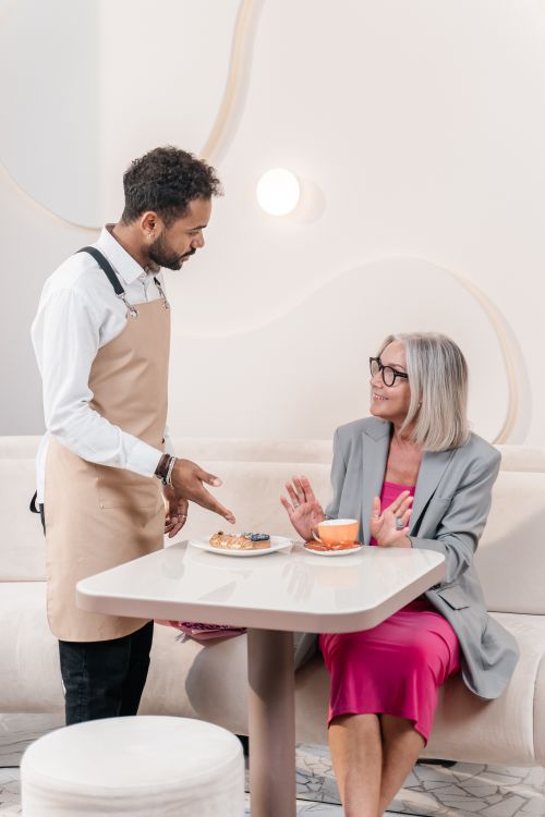 Free A waiter serves coffee and pastries to a senior woman at a modern indoor café. Stock Photo