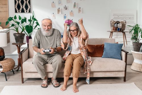 Free Elderly couple enjoying a fun gaming session together at home, smiling and celebrating. Stock Photo