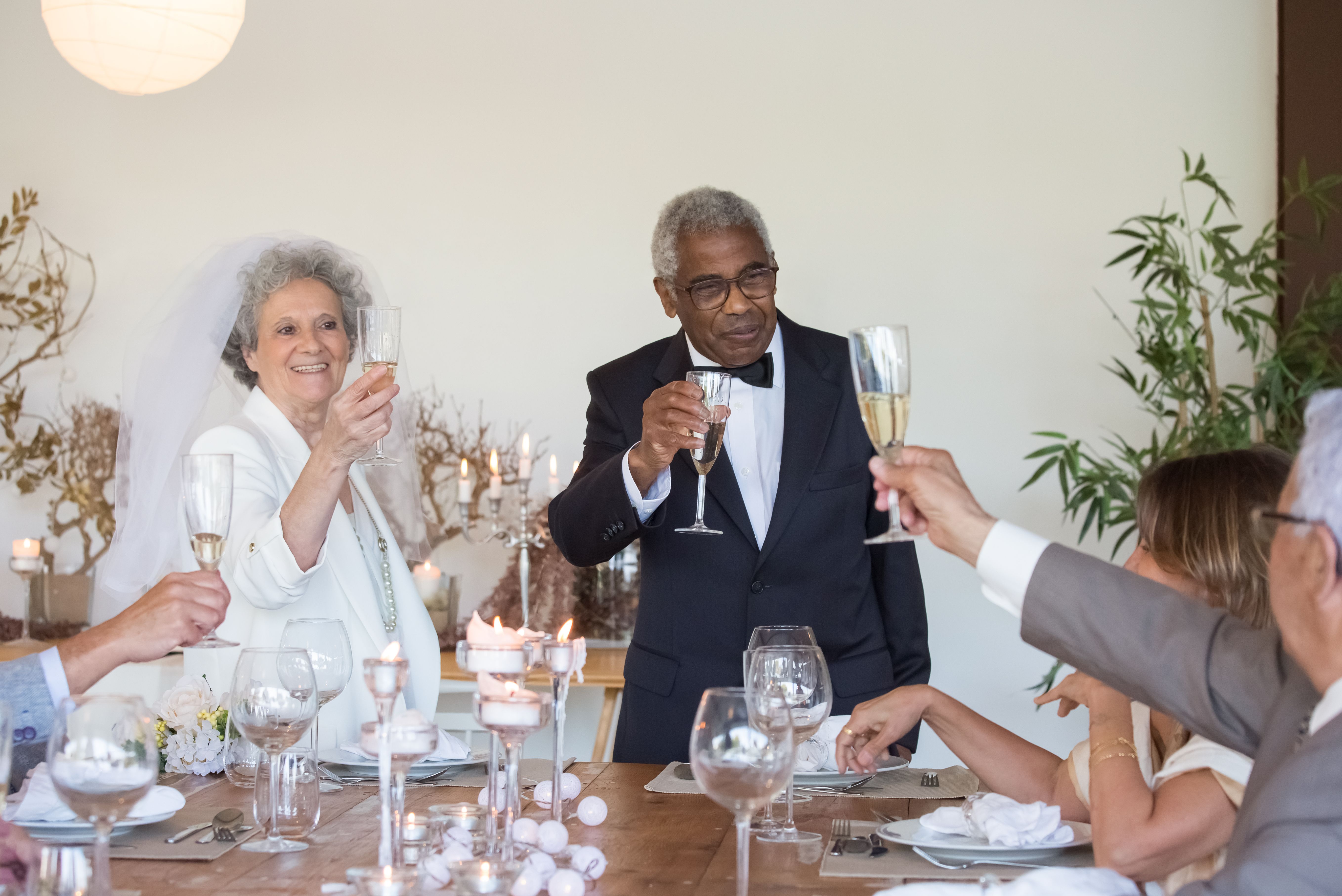 A happy senior couple celebrating their wedding with family and friends, toasting with champagne indoors.