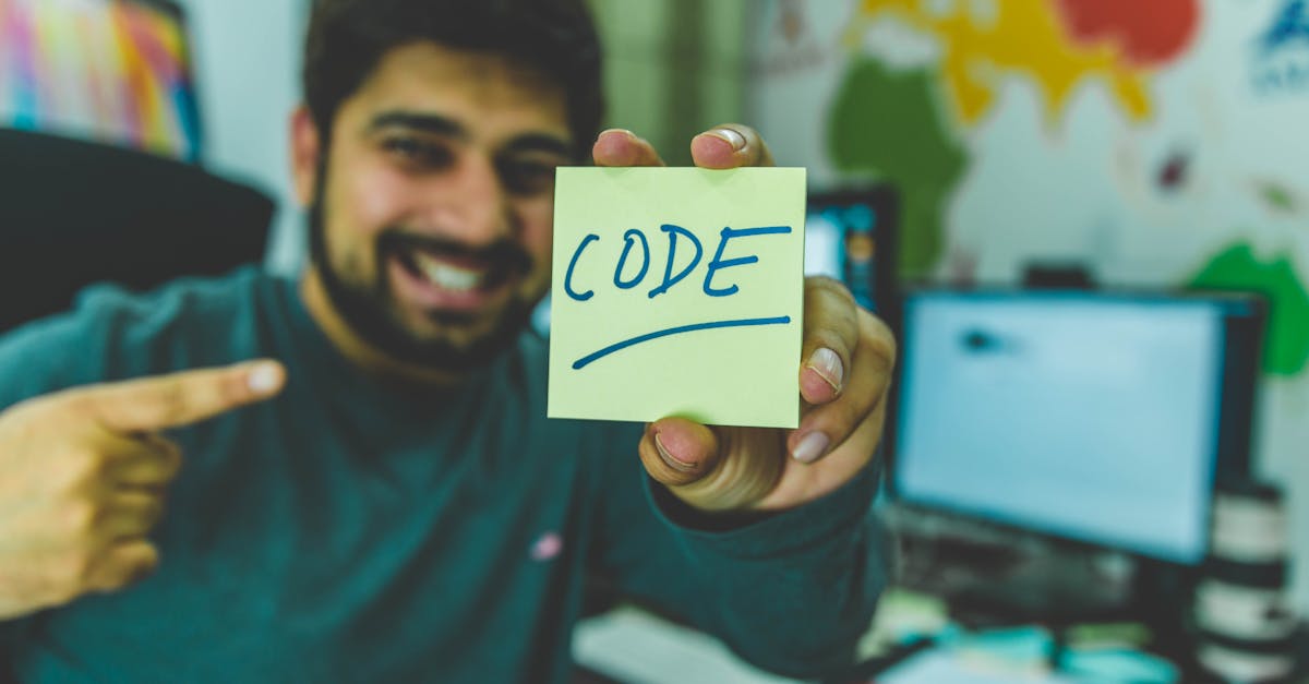 A smiling programmer pointing to a sticky note with 'code' written on it in an office setting.