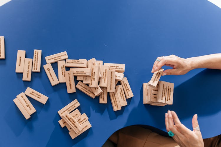 Person Stacking Wooden Blocks On Blue Table