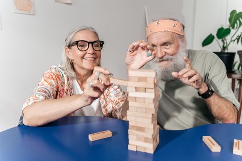 Free Senior couple enjoying a game of Jenga indoors, sharing laughter and fun. Stock Photo