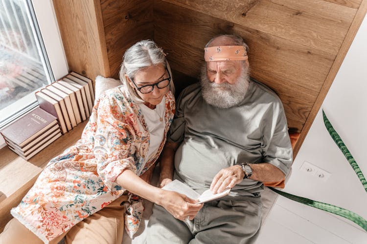 An Elderly Couple Lying On Bed Reading A Book