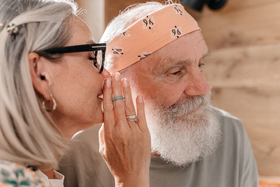 Older woman leaning in to speak into an older man's ear