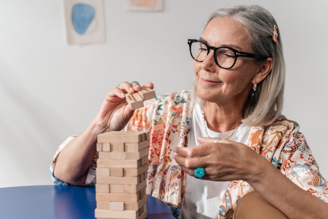 Close-Up Shot of an Elderly Woman with Eyeglasses Playing Jenga Blocks